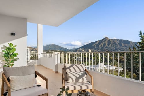 Marbella apartment terrace with mountain views, comfortable seating, and lush landscaping overlooking Nueva Andalucía