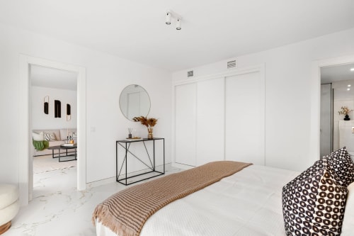 Modern Marbella bedroom with white marble floors, minimalist décor, round mirror, and patterned cushions