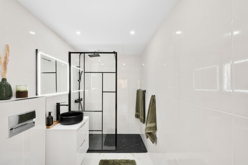 Modern bathroom at Marbella Home Rentals with black framed shower, white vanity, black sink, and marble floor