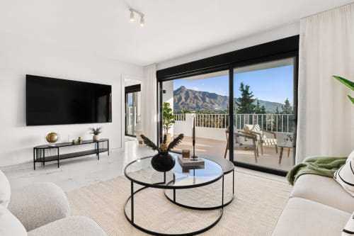 Modern Marbella apartment living room with mountain views, terrace, contemporary furnishings and black TV wall unit