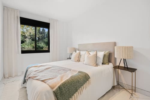 Bright bedroom in Marbella apartment with beige upholstered bed, decorative pillows, mountain view window, and modern