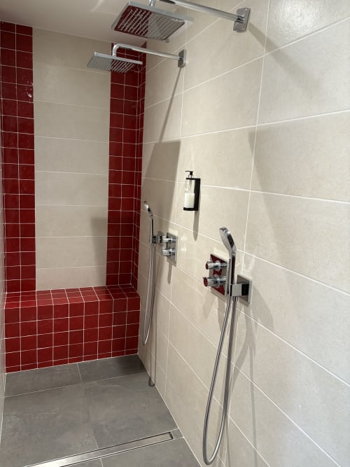 Douche moderne aux Chambres d'hôtes Lady Jule avec carrelage rouge, deux pommeaux de douche cascade et murs crème