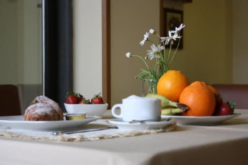 Tavolo da colazione elegante all'Hotel Milomax con pasticceria fresca, fragole, arance e fiori bianchi a Milo, Italia