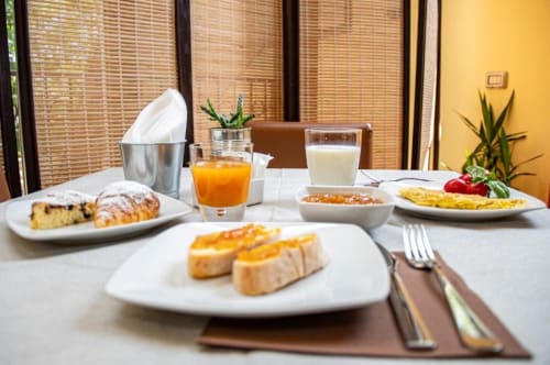 Colazione all'Hotel Milomax con French toast, frittata, dolci, succo e latte su piatti bianchi con pareti gialle