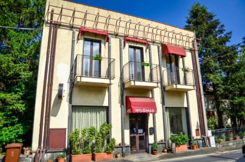 Facciata dell'Hotel Milomax a Milo con architettura Art Déco crema e rossa, balconi e tenda d'ingresso circondata dal verde