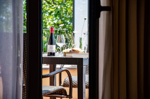Terrazza dell'Hotel Milomax con bottiglia di vino, bicchiere e stuzzichini che si affacciano sul giardino verde a Milo, Italia