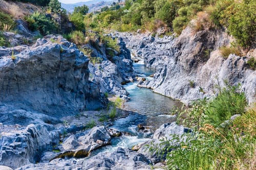 Türkisfarbener Fluss, der durch eine felsige Schlucht mit üppiger Vegetation fließt, in der Nähe des Hotels Milomax in Milo, Sizilien
