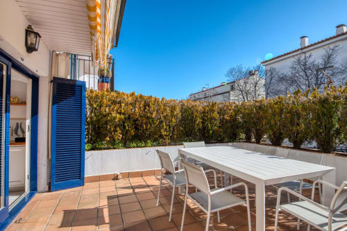 Sunny terrace with dining table, chairs, and hedges at beachfront apartment in Palafrugell, Spain