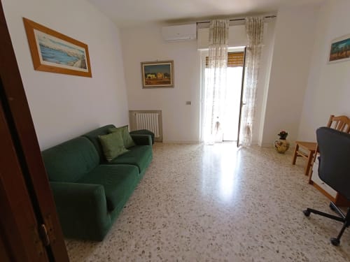 Ampio soggiorno in Casa Vacanze Alba, appartamento a Bari con divano verde, pavimento in terrazzo e accesso al balcone con vista mare