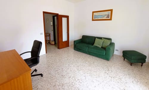 Ampio soggiorno in Casa Vacanze Alba, Bari con divano verde, scrivania e quadri con vista sul mare