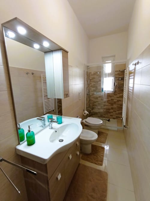 Bagno moderno a Bari Vacation con lavabo bianco, specchio illuminato, wc e doccia con parete in piastrelle marroni