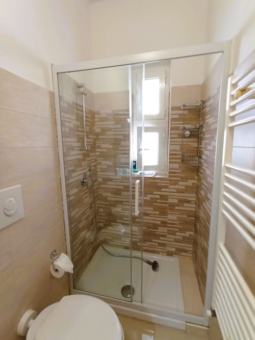 Moderna cabina doccia in vetro con pareti rivestite in piastrelle marroni nel bagno di Casa Vacanze Alba, Bari
