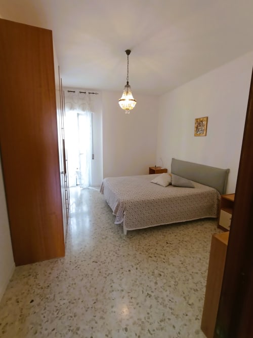 Ampia camera da letto in Casa Vacanze Alba, appartamento a Bari con letto, lampada a sospensione, porte in legno e pavimento in cotto