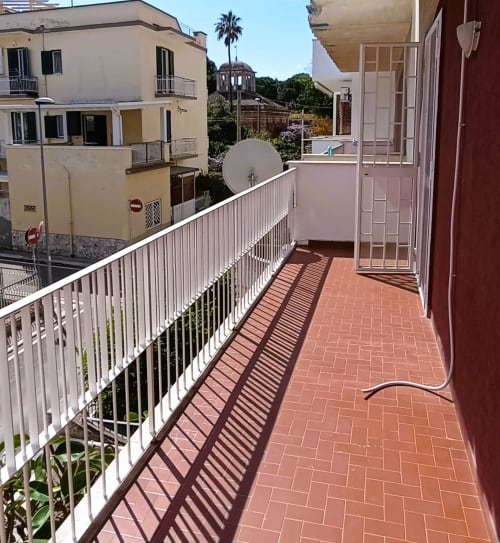 Ampio balcone dell'appartamento vacanziale a Bari con mattonelle in terracotta, ringhiera bianca e vista sul mare su edifici storici