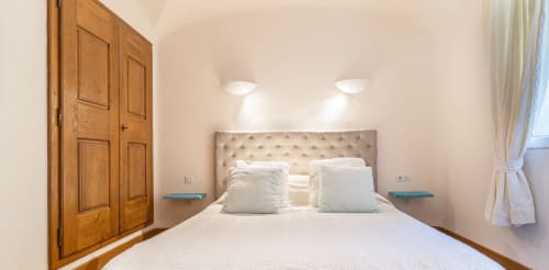 Chambre double lumineuse avec tête de lit tapissée beige, literie blanche, armoire en bois et appliques murales à Villa Marina Di