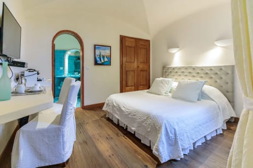Chambre lumineuse avec literie blanche, bureau, télévision et salle de bains à l'entrée turquoise arquée à la Villa Marina Di Cavu, Bonifacio