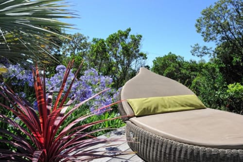 Lit de jour luxueux avec coussin vert citron, entouré de fleurs violettes et plantes tropicales à la Villa Marina Di Cavu à Bonifacio