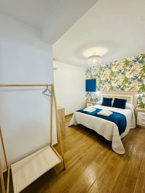 Dormitorio moderno en Mérida con papel tapiz tropical, piso de madera, acentos azules y vista de la ciudad
