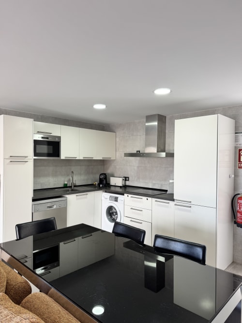 Cocina moderna con gabinetes blancos, encimeras negras y electrodomésticos de acero inoxidable en el apartamento El Faro De Los Genoveses,