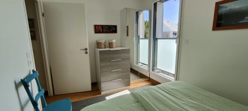Chambre lumineuse à Mer et Maisons avec literie verte, commode en bois, portes vitrées donnant sur balcon avec vue sur La Trinité sur Mer
