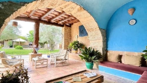 Terraza de Can Gat Vell con estructura de arco de piedra, pérgola de madera y muros azules en Girona, Empordà