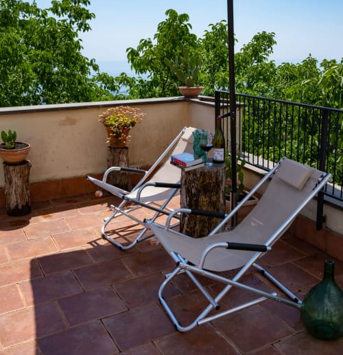 Terrazza soleggiata dell'Hotel Milomax con lettini, piante in vaso, bottiglie di vino e viste panoramiche sulla campagna verde.