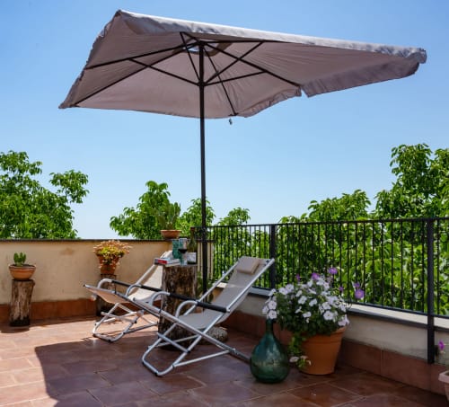 Terrazza panoramica dell'Hotel Milomax con lettino, ombrellone color tortora, fiori in vaso e ringhiera ricoperta di edera a Milo, Italia