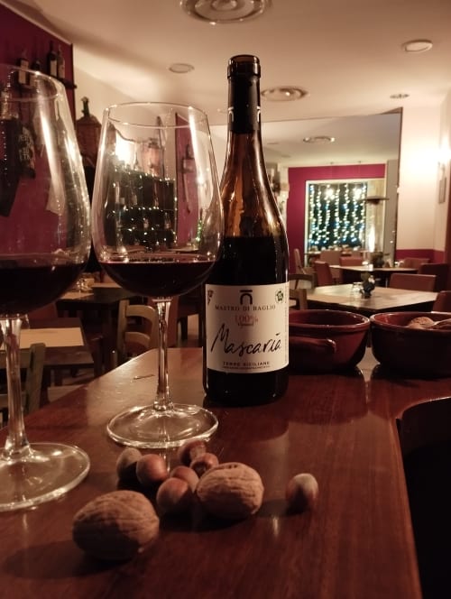 Bottiglia di vino Mascaraia siciliano con bicchiere all'Hotel Milomax a Milo, CT, accompagnato da frutta secca e un'atmosfera culinaria elegante