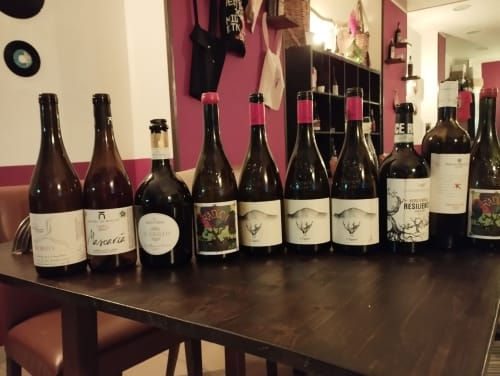 Bottiglie di vino esposte su tavolo scuro nella sala degustazione dell'Hotel Milomax a Milo, Italia, con pareti rosa antico