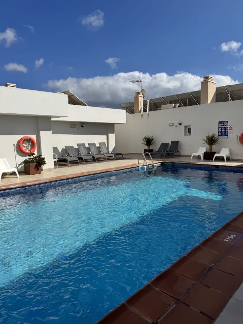 Zona de piscina de El Faro De Los Genoveses con hamacas, edificios blancos y cielo azul en San José, Almería