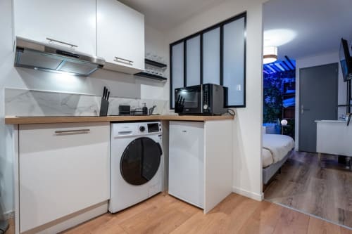 Modern kitchen with washing machine in Bordeaux apartment at Wellkhome, featuring white cabinets and wood countertops