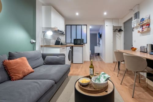 Modern apartment living area at Wellkhome Bordeaux with gray sofa, kitchen, work desk, and city view