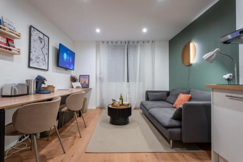 Cozy Wellkhome apartment in Bordeaux with grey sofa, wooden desk, green accent wall, and modern amenities including TV and