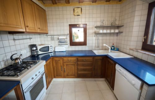 Cocina con encimeras azules, armarios de madera y salpicadero de azulejos blancos en Can Gat Vell B&B, Girona, Cataluña