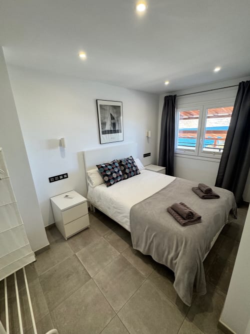 Habitación moderna en El Faro De Los Genoveses con vista al mar, cama blanca, mesita de noche y paisaje costero visible