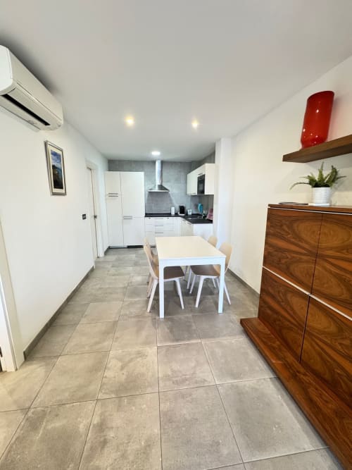Moderna cocina-comedor del apartamento El Faro De Los Genoveses con mesa blanca, muebles de madera y pisos de baldosa