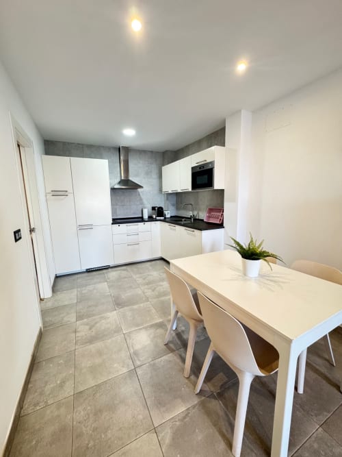 Moderna zona de cocina-comedor en el apartamento El Faro De Los Genoveses, San José, Almería con muebles blancos y pisos de azulejos