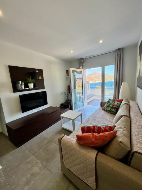 Luminoso salón con vistas al mar, sofá beige, TV de pantalla plana y vista al Mediterráneo en El Faro De Los Genoveses