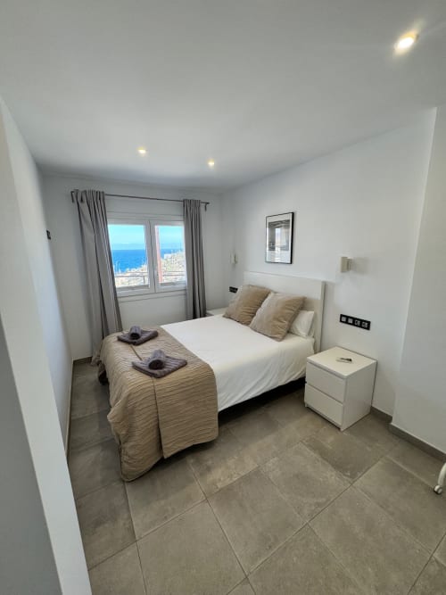 Moderno dormitorio en El Faro De Los Genoveses con cama blanca, vistas al mar y paisaje costero visible desde la ventana en San José