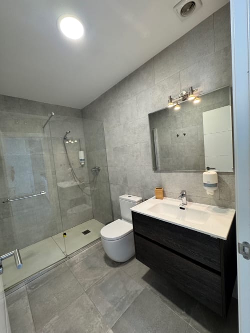 Baño moderno con azulejos grises, mueble oscuro, lavamanos blanco, inodoro y ducha caminable en El Faro De Los Genoveses, San José
