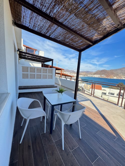 Terraza frente al mar con sillas blancas, mesa y sombrilla tejida en El Faro De Los Genoveses, San José, Almería