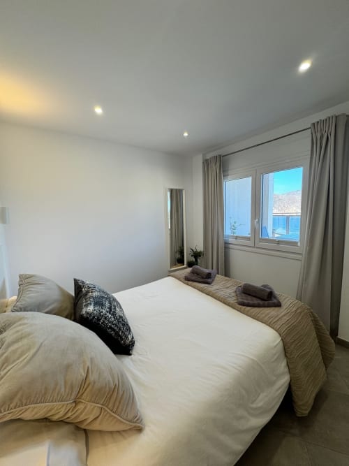 Dormitorio moderno en El Faro De Los Genoveses con vistas al mar, ropa de cama blanca y ventanal costero en San José, Almería