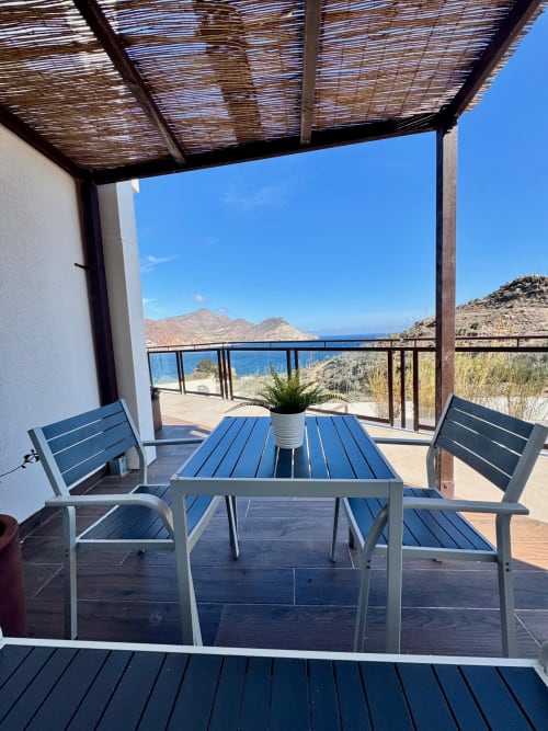 Terraza costera en El Faro De Los Genoveses con mesa de comedor, sillas azules, vistas al mar y montañas en Almería