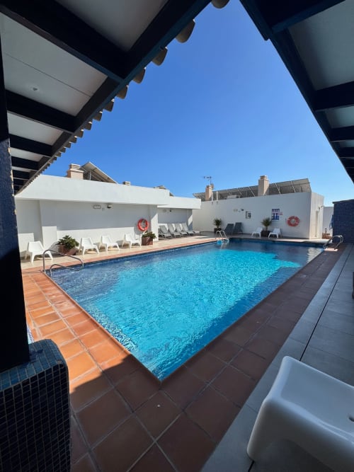 Soleada zona de piscina del hotel El Faro De Los Genoveses en San José, Almería con agua azul cristalina, tumbonas blancas y pérgola