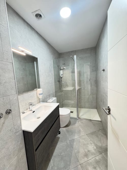 Baño moderno del apartamento El Faro De Los Genoveses, San José Almería con azulejos grises, lavabo, inodoro y ducha a ras de suelo