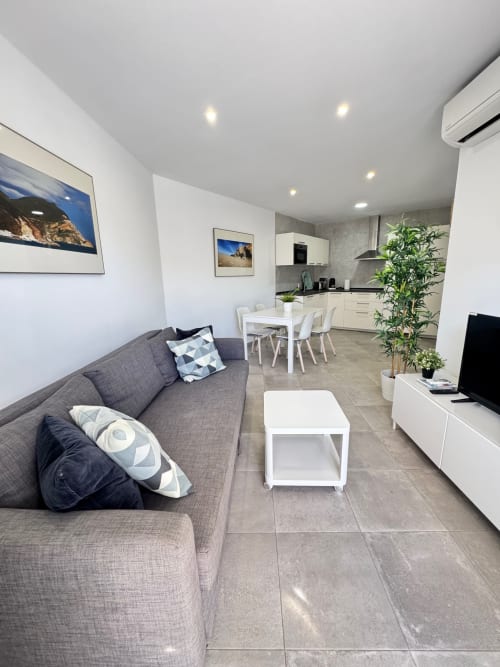 Moderna sala de estar en El Faro De Los Genoveses con sofá gris, comedor blanco, cocina y cuadros con vista al mar