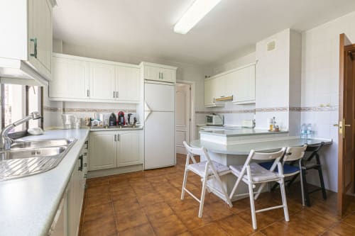 Modern kitchen and dining area in Marbella apartment with white cabinetry, stainless steel appliances, and terracotta tile