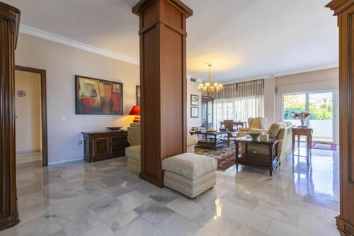 Spacious Marbella apartment living room with marble floors, wooden columns, elegant furnishings and garden views