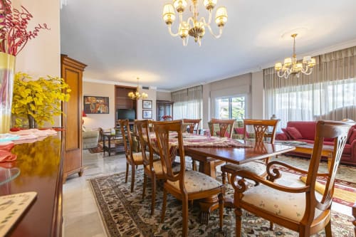 Elegant dining room with wooden table and chairs, chandeliers, and lounge area in Marbella apartment