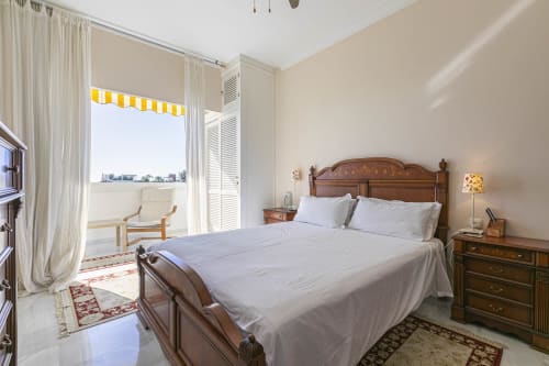 Bright Marbella apartment bedroom with wooden bed, terrace access, and pool view in Nueva Andalucía